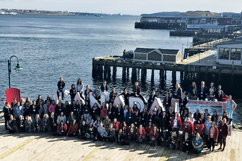 a large group of women posing for a photo on a pier in halifax